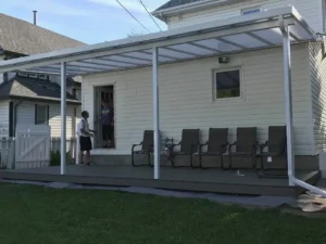 A man stands under an Acrylic Patio Cover, surrounded by chairs, showcasing the product's design and functionality.