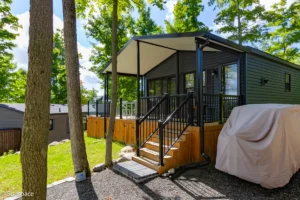 A small cabin with a deck and a car parked in the driveway, showcasing RV/Resort Living features.
