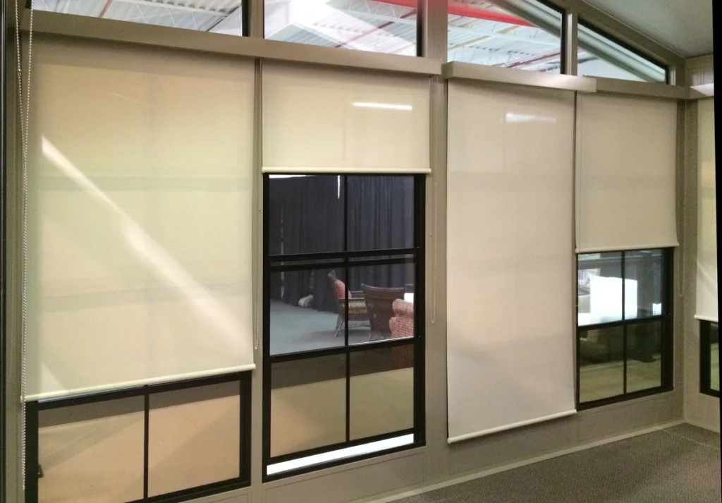 Interior view featuring sunshade roller blinds on large glass windows and a black-framed glass door.