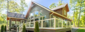 House in the woods featuring a deck and porch, showcasing Aluminum Railing with Glass for a modern touch.