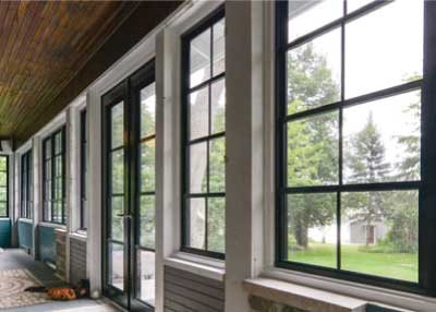 Long Sunroom with black-framed windows and a dark wood ceiling, overlooking a grassy yard.