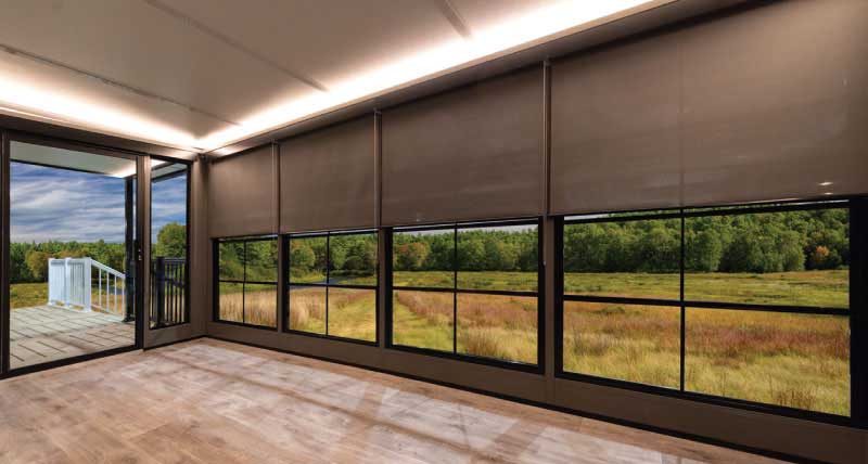 Room interior with modern Sunshades partly covering large windows, showing a green yard and patio.