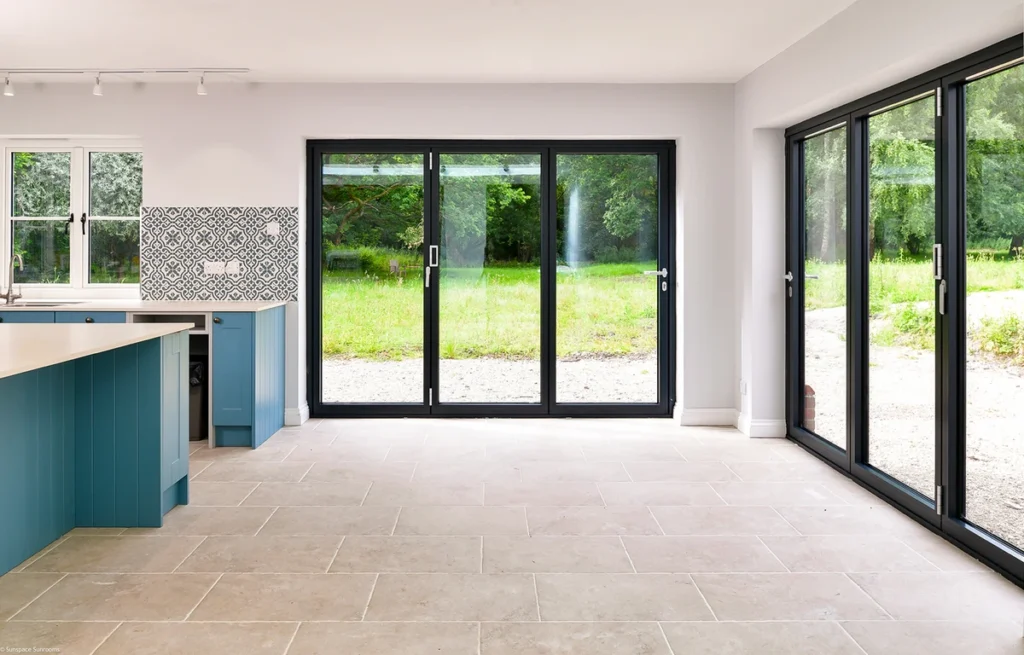 A contemporary kitchen with a blue island and WeatherMaster™ Plus Bi-Fold doors opening to an outdoor area.