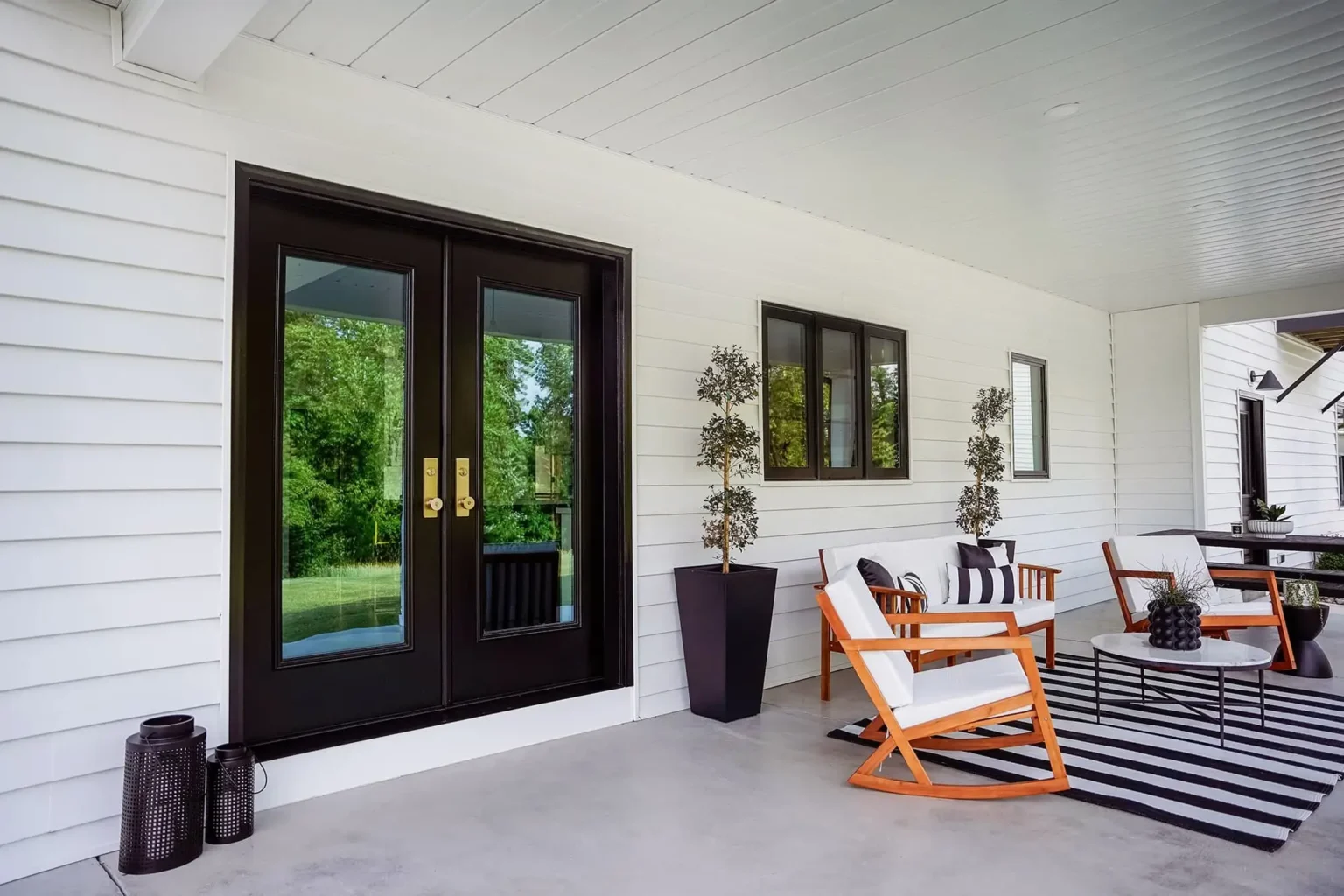 WeatherMaster™ black French doors with glass panels and gold handles, set against a white exterior wall.