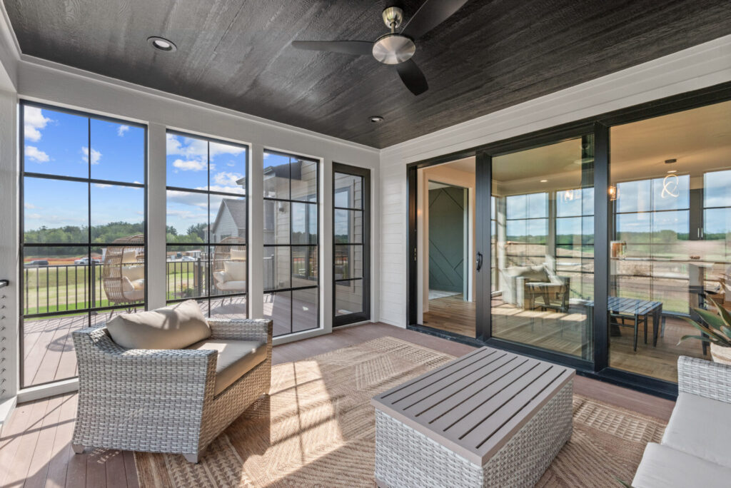 A bright sunroom featuring wicker furniture and large glass doors, showcasing Porch Conversions' stylish design.