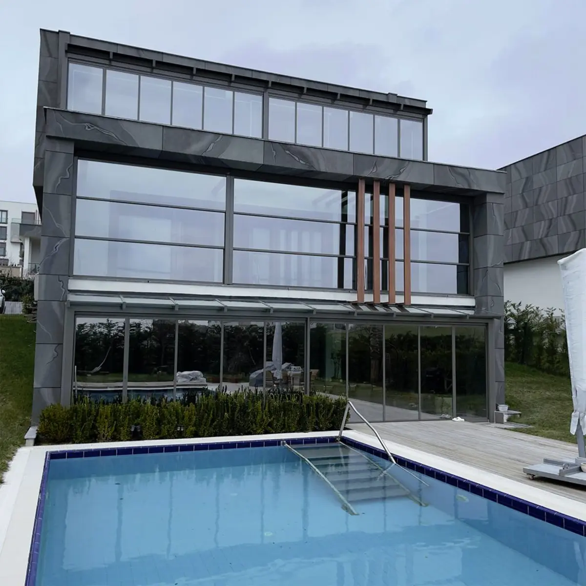 Modern house with a large glass wall and pool, showcasing sleek contemporary architecture and design.