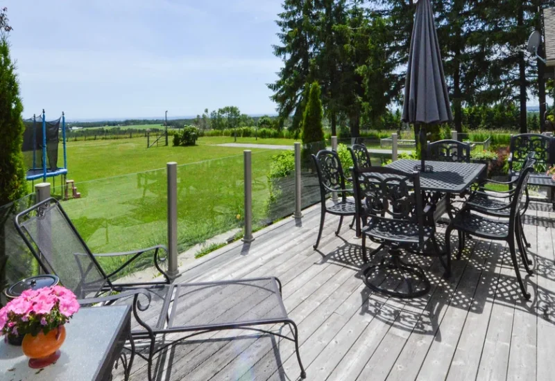 Deck with chairs and tables overlooking a field, featuring Topless Glass Railing for unobstructed views.