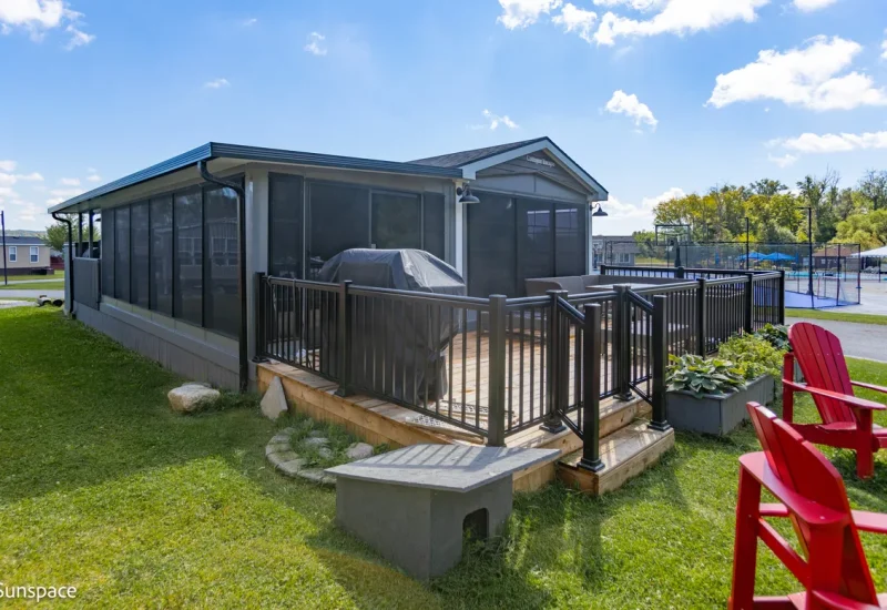A small house with a deck featuring two red chairs, showcasing RV/Resort Living product design.
