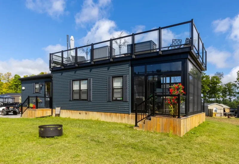 A tiny house with a deck sits on green grass, showcasing RV and resort living in a serene outdoor setting.