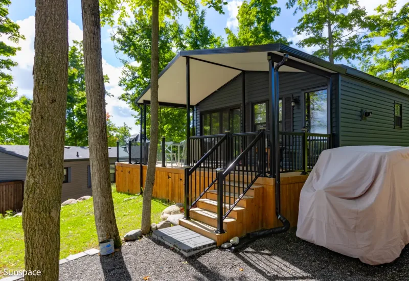 A small cabin with a deck and a car parked in the driveway, showcasing RV/Resort Living features.