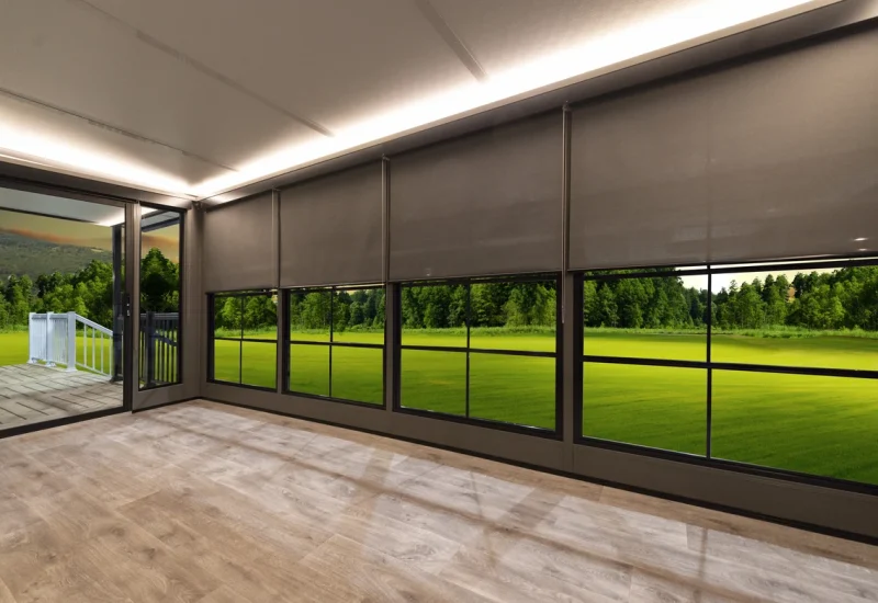 Modern sunshades partially drawn over large windows, revealing a patio and green landscape.