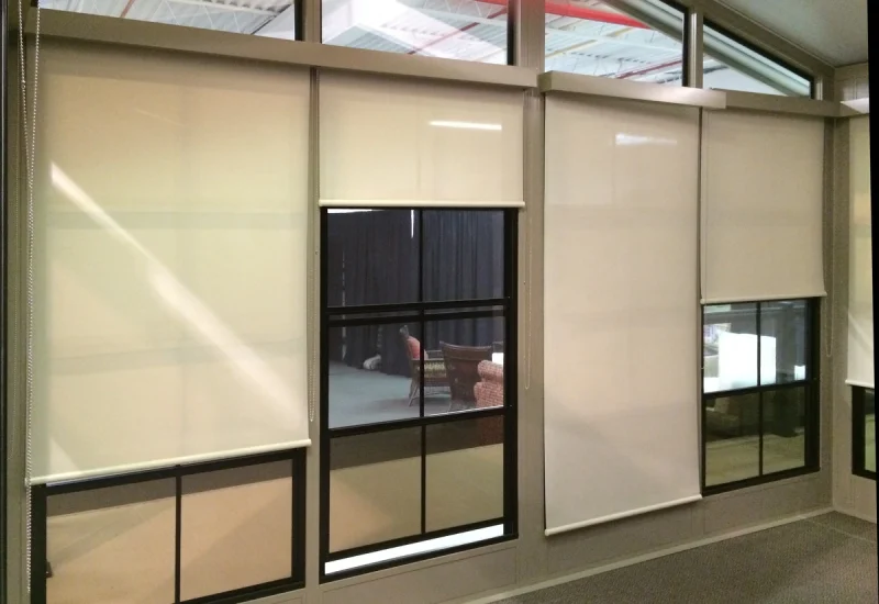 Interior view featuring sunshade roller blinds on large glass windows and a black-framed glass door.