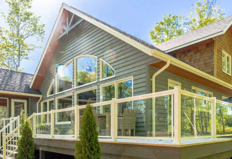 House in the woods featuring a deck and porch, showcasing Aluminum Railing with Glass for a modern touch.