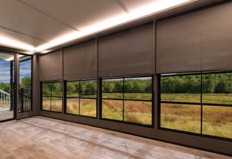 Room interior with modern Sunshades partly covering large windows, showing a green yard and patio.