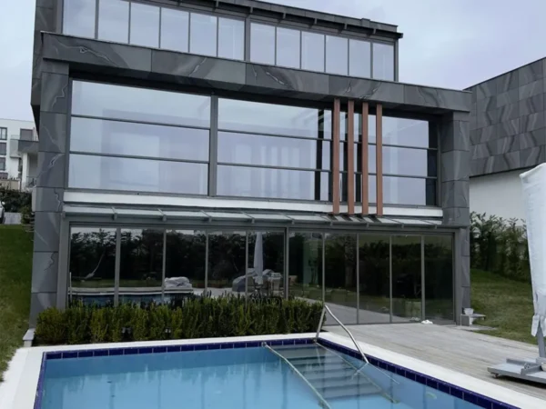 Modern house with a large glass wall and pool, showcasing sleek contemporary architecture and design.