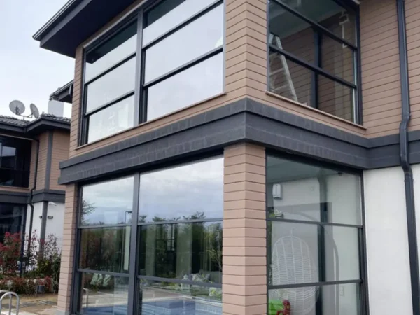 A modern house with large windows and a swimming pool, set in a bright and sunny outdoor setting.