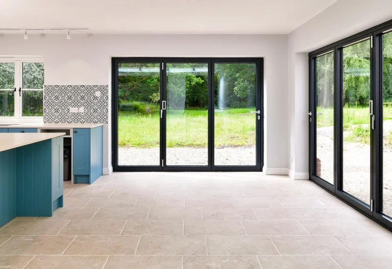 A contemporary kitchen with a blue island and WeatherMaster™ Plus Bi-Fold doors opening to an outdoor area.