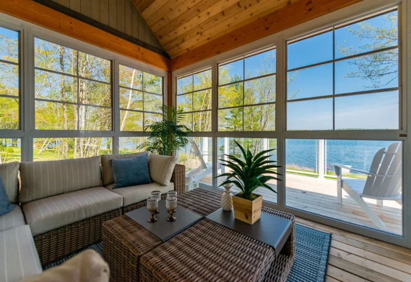 Bright Sunroom with wicker seating and expansive windows overlooking tranquil water, showcasing WeatherMaster™ Windows & Doors.